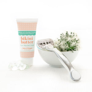 Luxe Shaving Cream Bikini Cutter scented with Mixologie Tempted (Coconut Kiss) Fragrance in a 2 fl oz or 60 mL white tube with orange circle pattern and white cap. Bikini Butter pictured with white background pebbles, a cactus, and razor. 